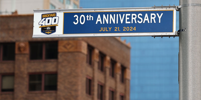 A street sign showing "30th Anniversary July 21, 2024" beside the 2024 Brickyard 400 logo