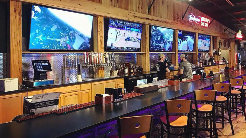 Multiple large screens showing live sports over a bar tabletop