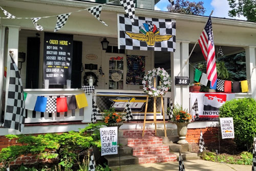 Many Indianapolis Motor Speedway decorations including flags and signs on the front porch of a white house