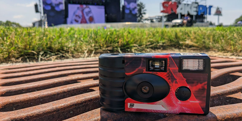 Detail image of the front of a point-and-shoot camera sitting on a grate in front of the Snake Pit sign