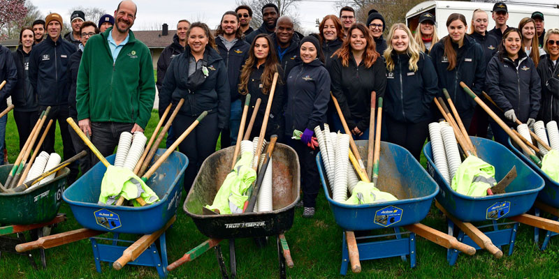 Penske Entertainment employees pose with wheelbarrows and shovels before planting trees