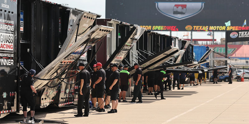 INDYCAR car haulers and crew members setting up in the garage area at Texas Motor Speedway